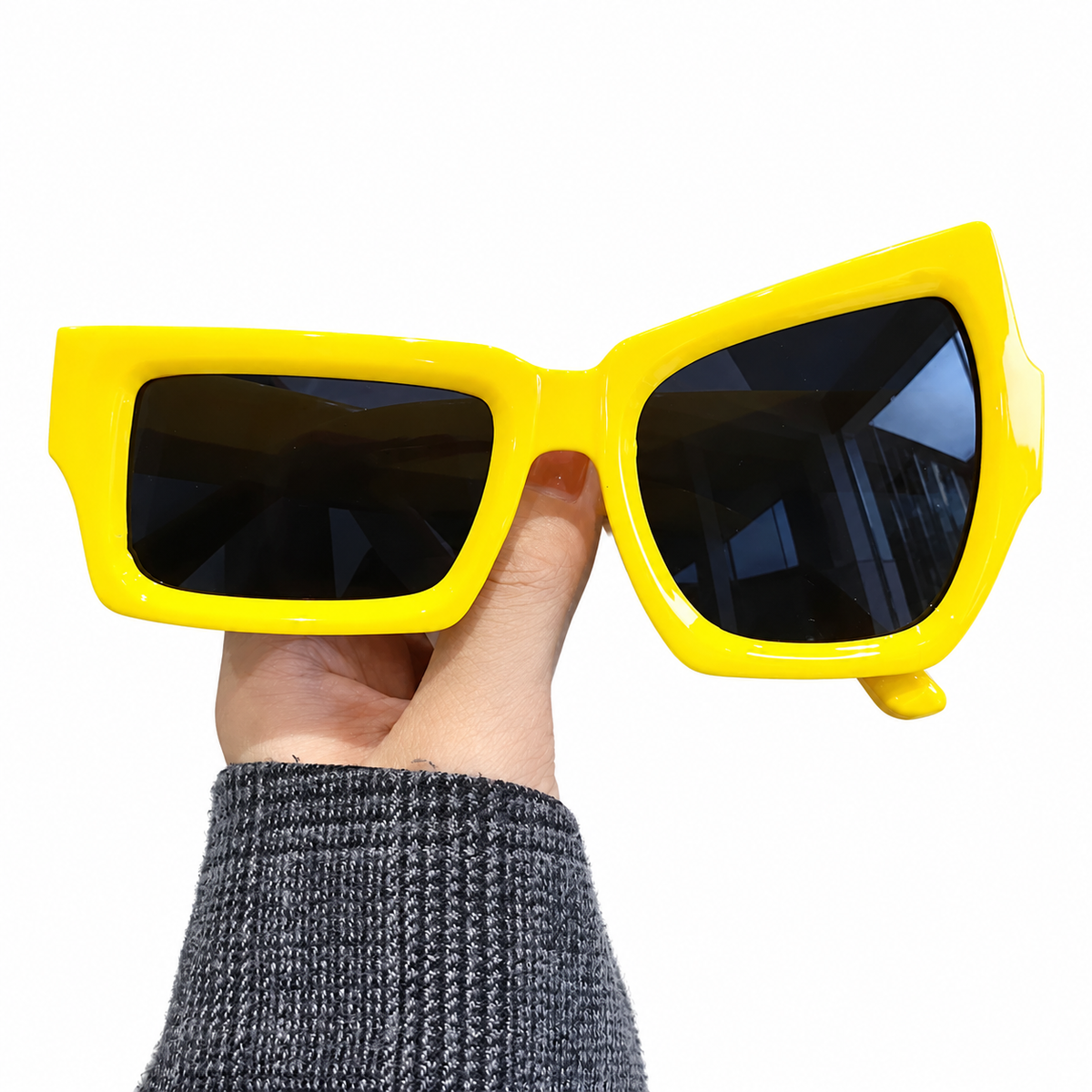 Lunettes fantaisie asymétriques jaunes présentées à la main.